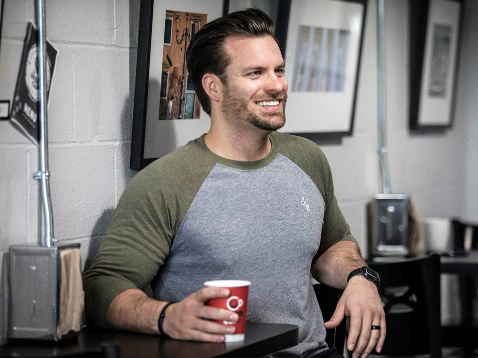 Man having coffee in a grey and green raglan. 