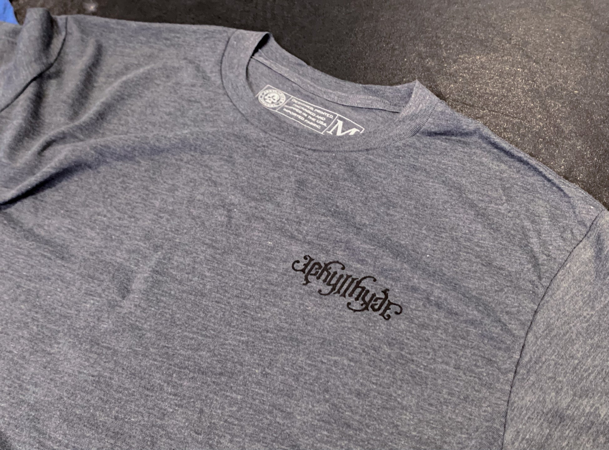 Grey tshirt on a black rubber floor with a jekyllhyde logo on the left chest. 