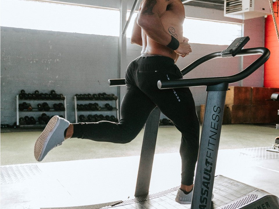 Man running on a treadmill shirtless with black joggers.