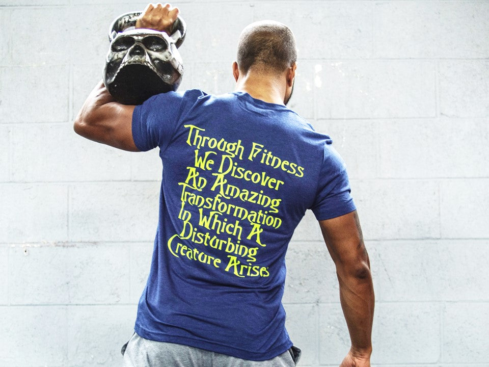 Man with a skull kettlebell facing a wall in a blue tshirt. 