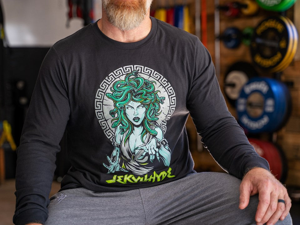 Man sitting with his hand on his knee wearing a long sleeve shirt with medusa on the front. 