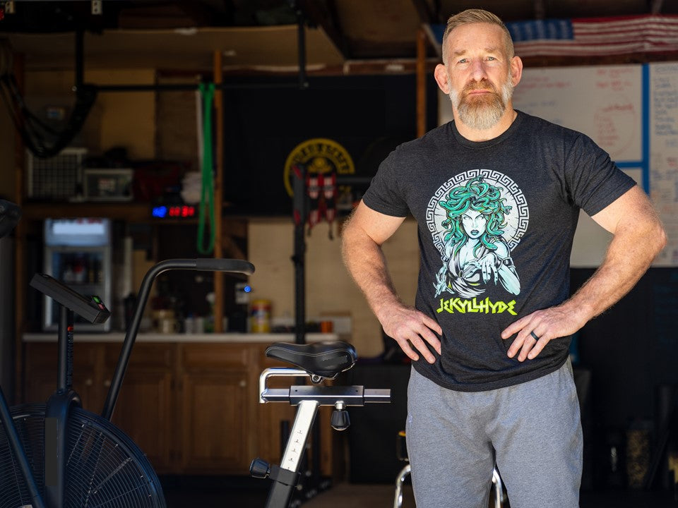 Man standing in a garage gym wearing a black shirt with Medusa on it. 