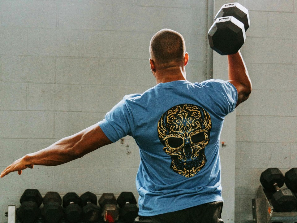Man with dumbbell wearing a blue shirt with a sugar skull. 