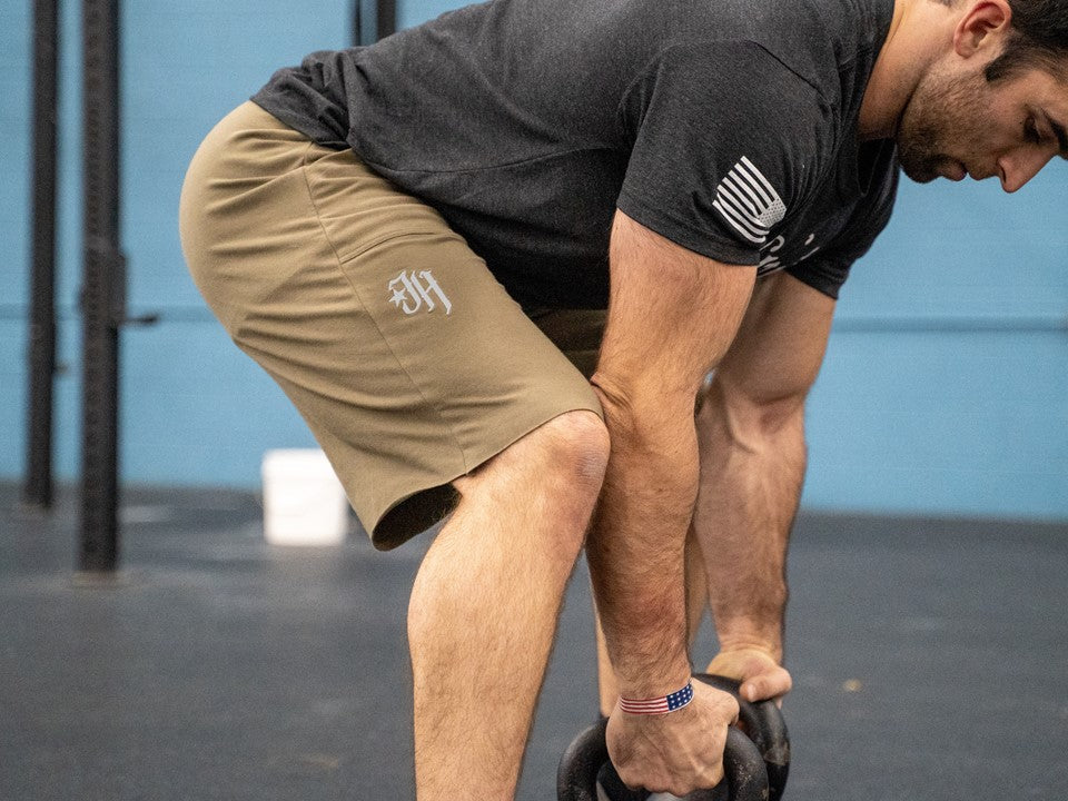 A man grabbing kettlebells wearing od green shorts. 