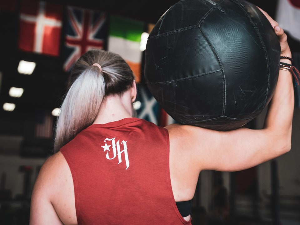 Woman with her back to the camera holding a medicine ball on her shoulder. 