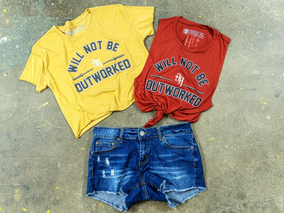 Gold crop top and rust muscle tee lying on concrete floor with jean shorts. 
