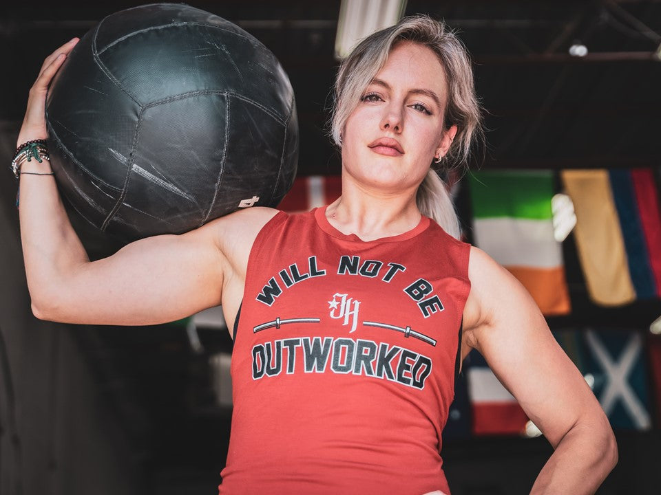Woman holding a medicine ball n her shoulder in a rust muscle tee