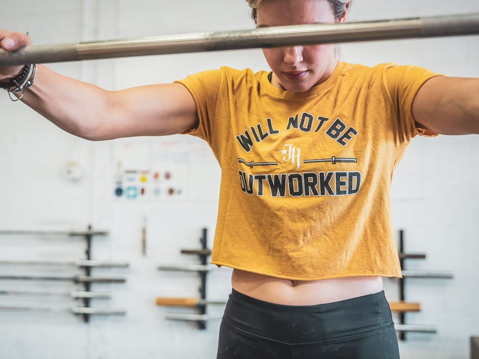 Woman standing at a barbell in a gold crop top