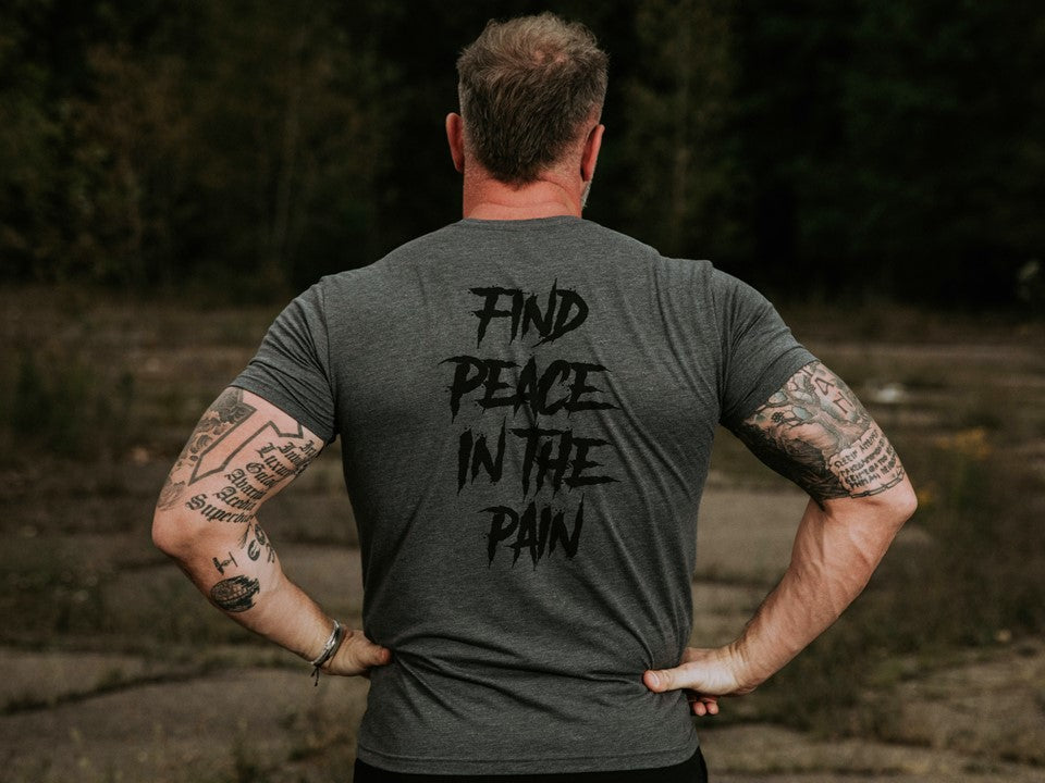 Muscular man in a grey shirt with the words "Find Peace in the Pain" on the back. 