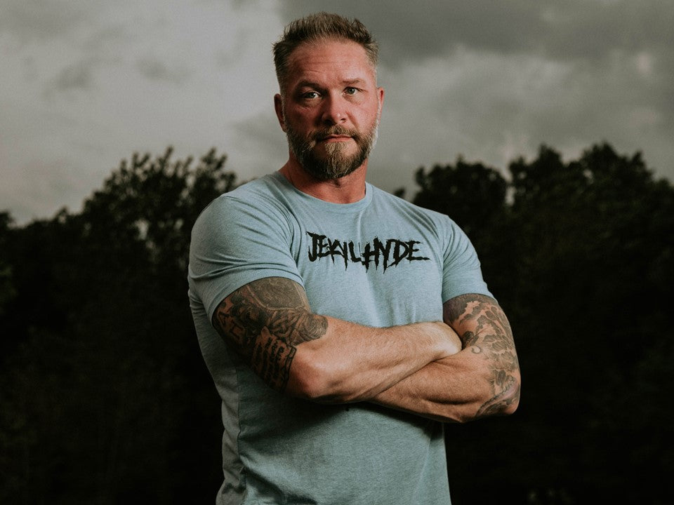 Man with his arms crossed wearing a blue shirt with Jekyllhyde across the chest. 