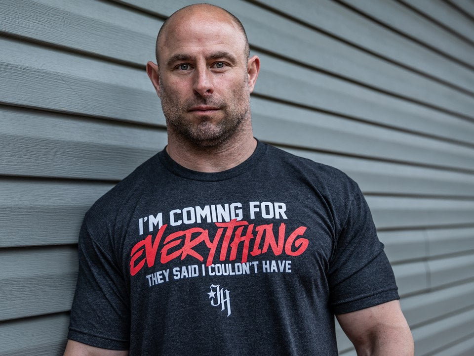 Man leaning against a house wearing a black shirt with a motivational saying on it. 