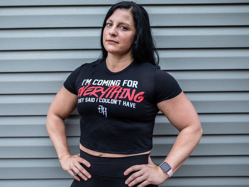 Woman standing against a wall wearing a black crop top. 