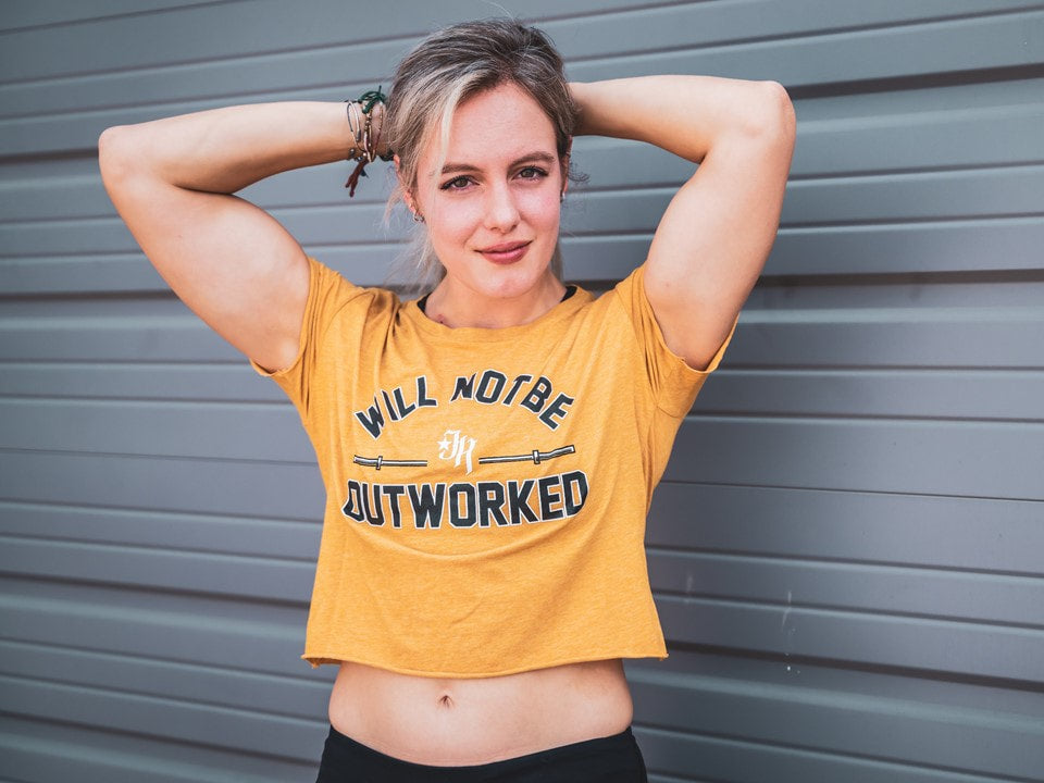 Woman standing against a grey background wearing a gold crop top. 