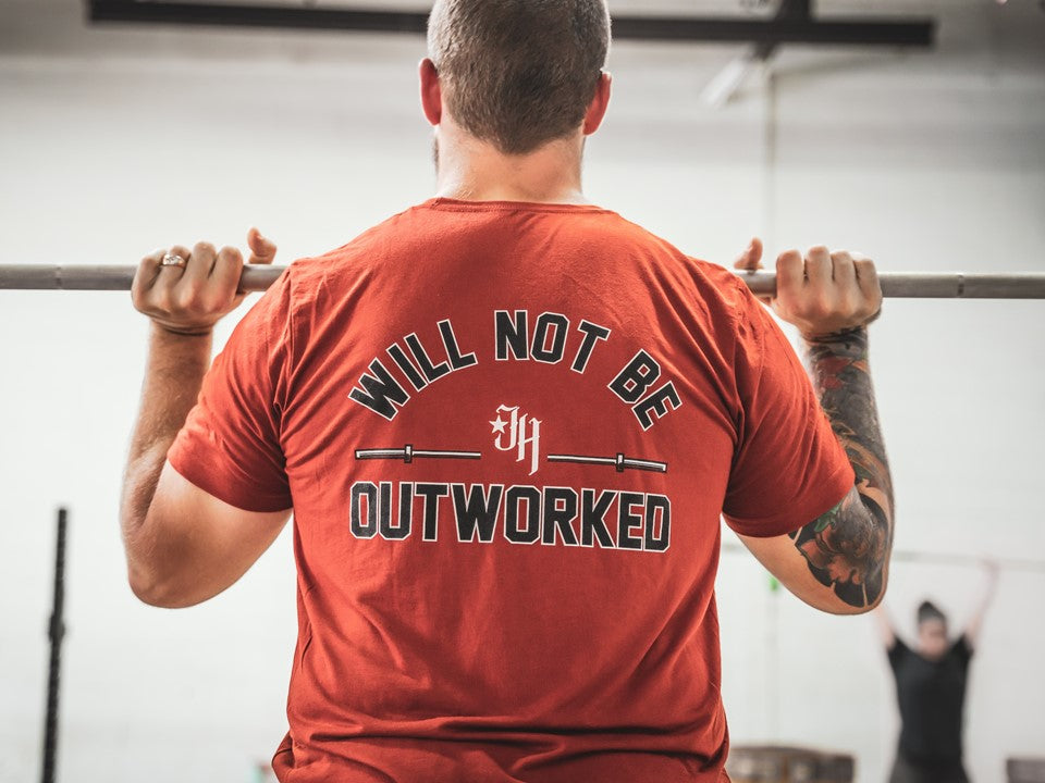 Man in rust colored shirt with back to camera holding a barbell. 