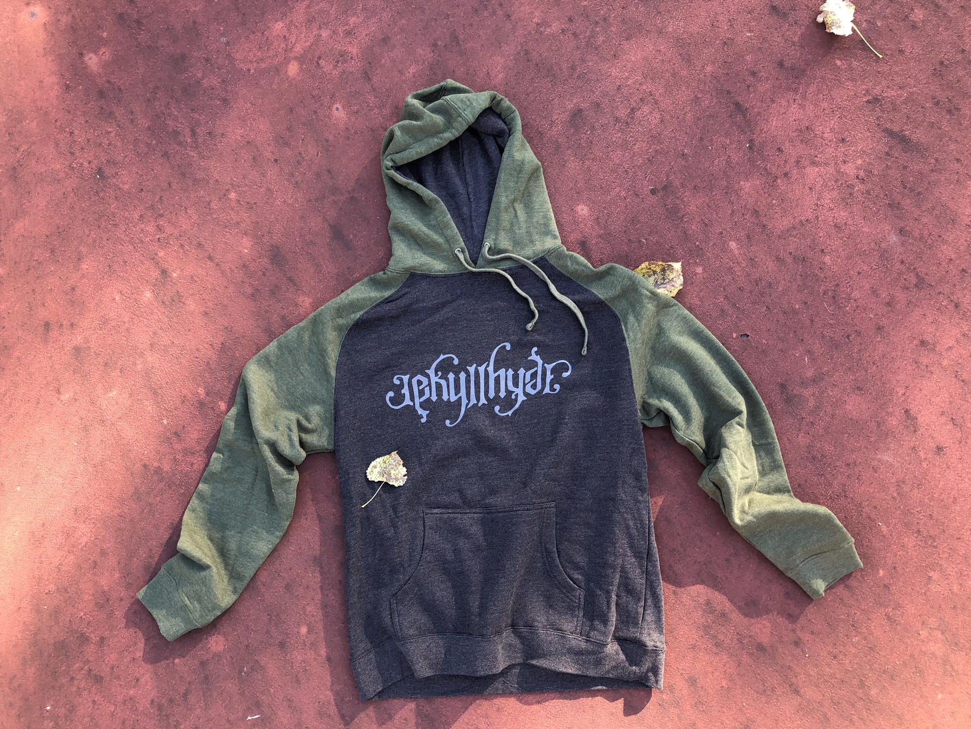 Green and charcoal hoodie on a reddish floor. 