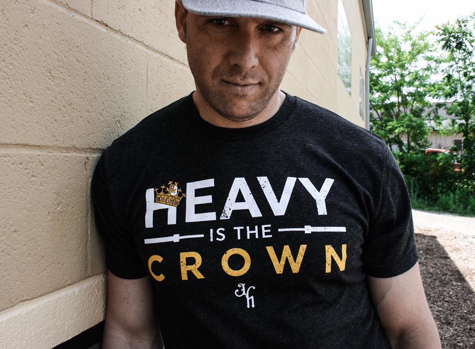 man leaning against the wall with a shirt that reads "Heavy is the crown"