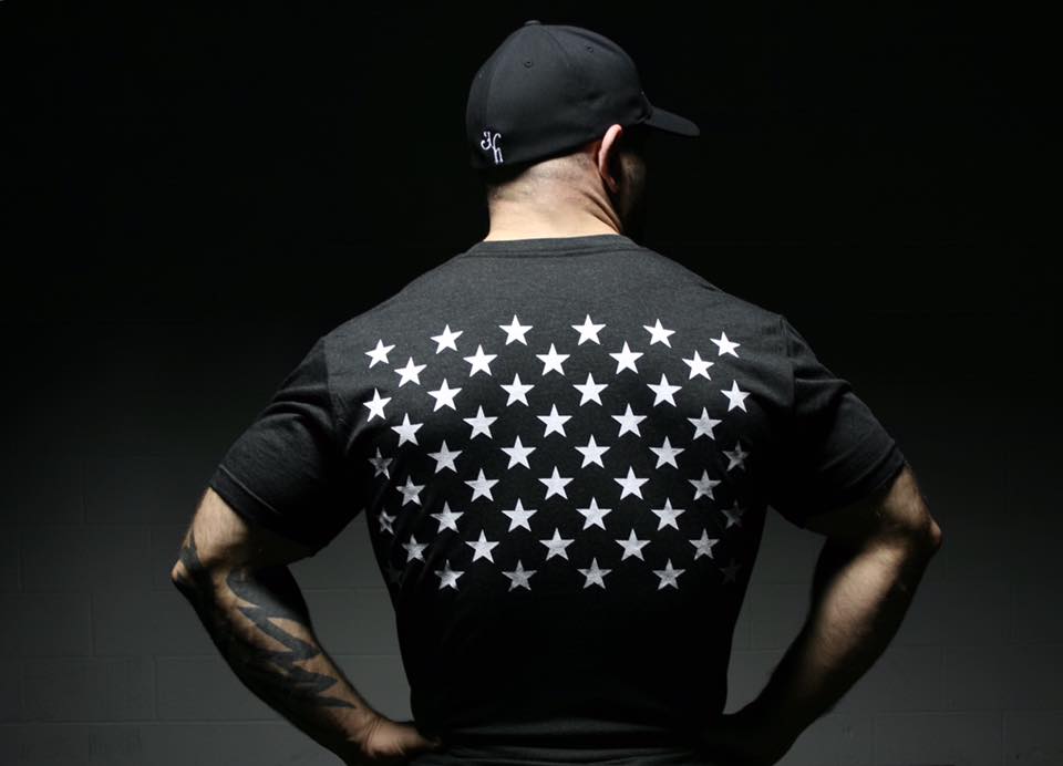 Man standing with back to the camera, looking to the right wearing a black shirt with 50 stars on the back. 