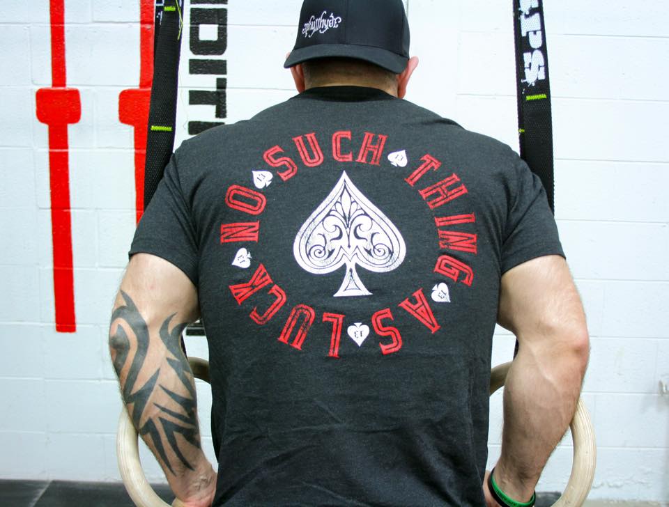 Man doing dips on rings in a black shirt with text and spades on it. 