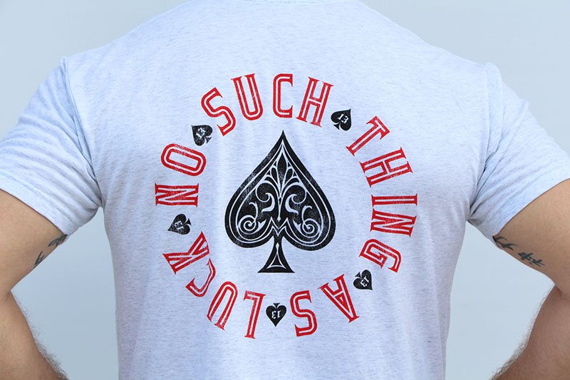 Close up of a heathered white shirt that reads "No Such Thing As Luck" 