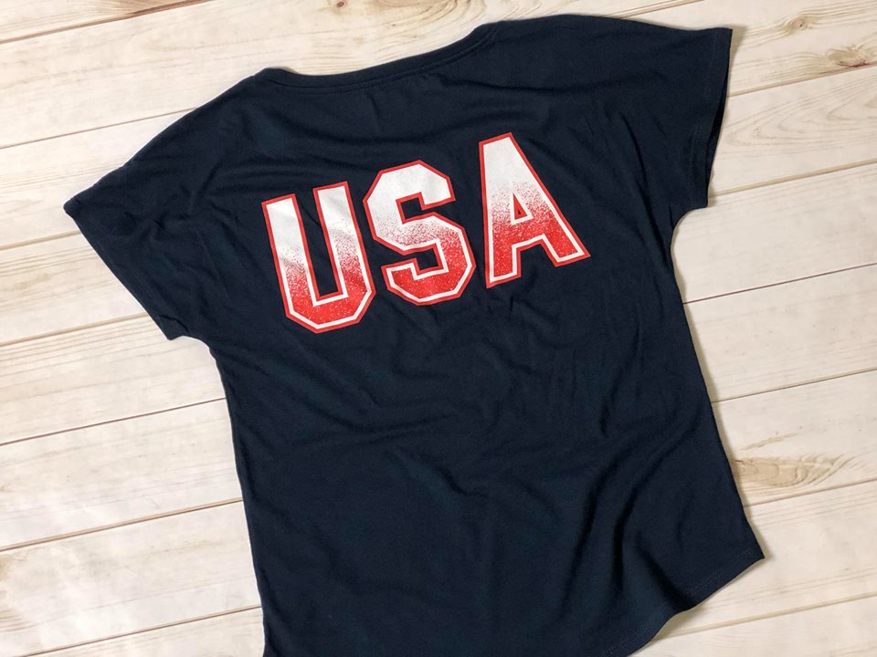 Navy shirt with USA on it laying on a wood floor. 