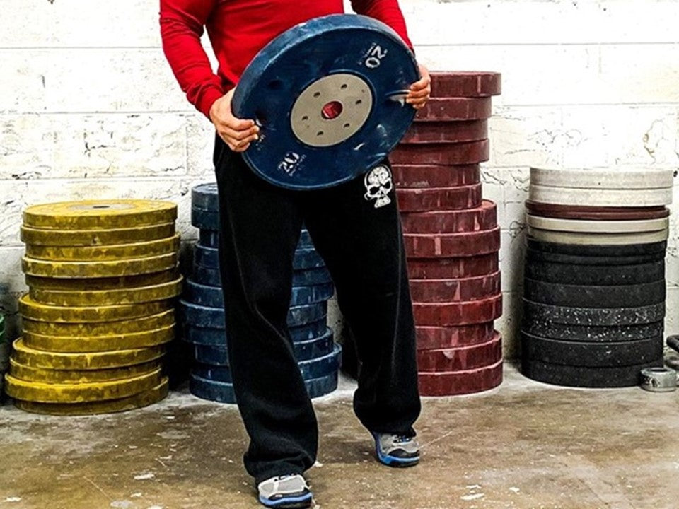 Person holding a 20 kg plate wearing black sweatpants. 