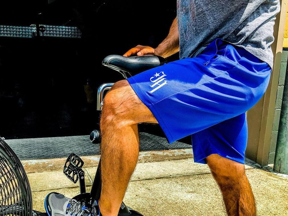 Blue shorts on a man standing next to an exercise bike. 