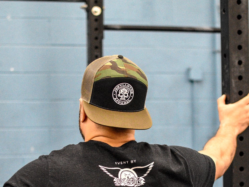 Man standing at a pullup rig with a backwards hat on that has a skull. 