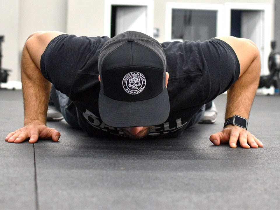 Man doing a burpee in a skull trucker hat. 
