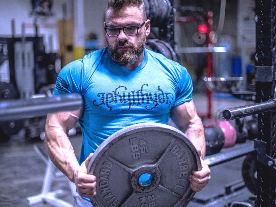 Muscular man in turquoise tshirt holding a 45 lb plate. 