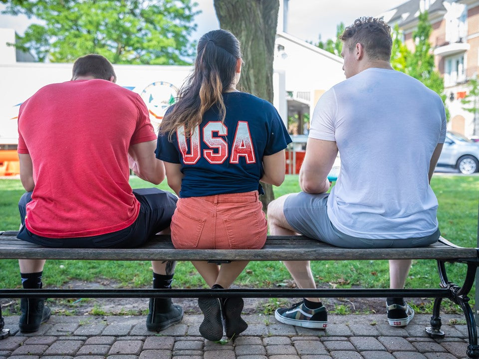 3 people sitting on a park bench with their backs to the camera. 