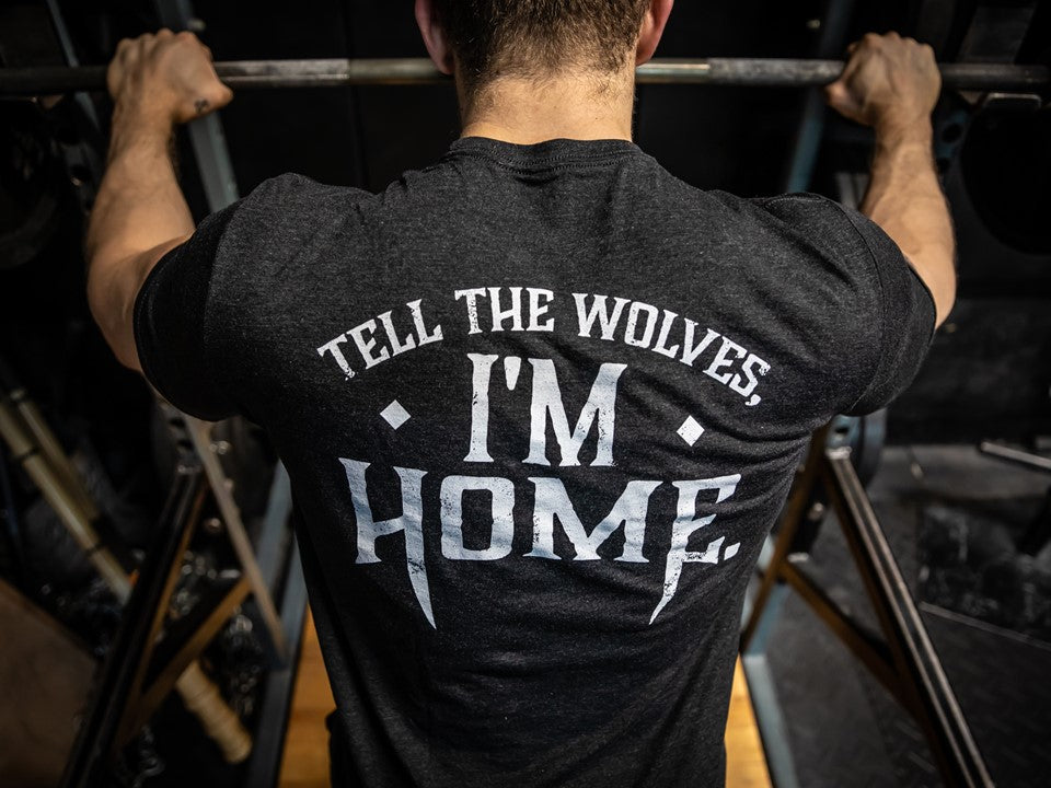 man standing at a barbell in a black shirt with slogan. 